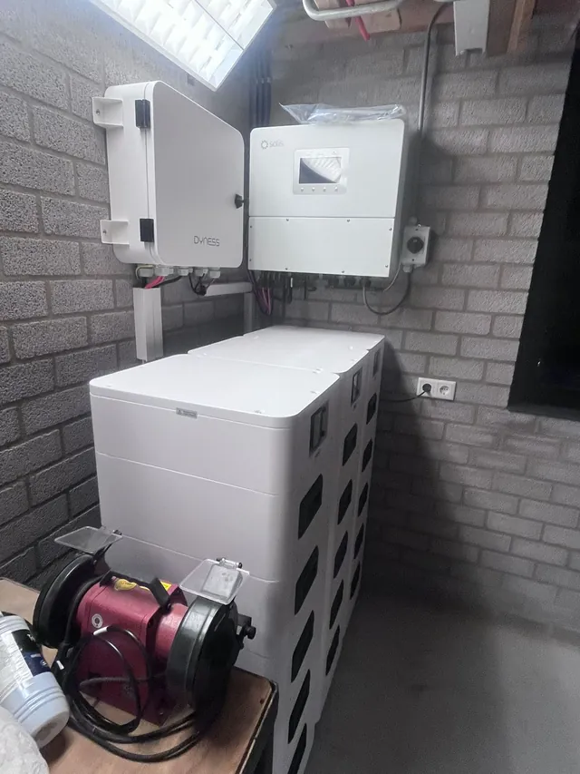 Zijaanzicht van drie Dyness-batterijtorens met een Dyness-aansluitkast en Solis-omvormer aan de muur.