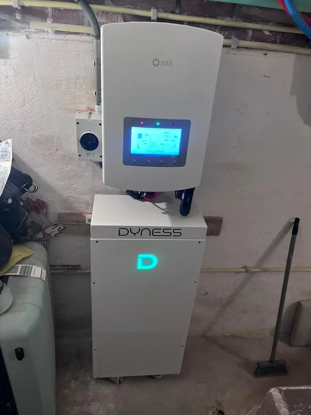 Solis-omvormer met ingeschakeld display, gemonteerd boven een Dyness-batterijkast met verlicht logo.